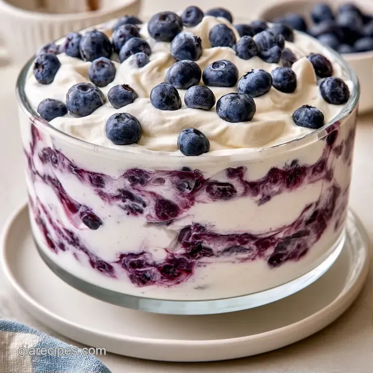 A tall glass parfait showing distinct layers of creamy custard, soft cake, and a glossy, deep purple berry compote.