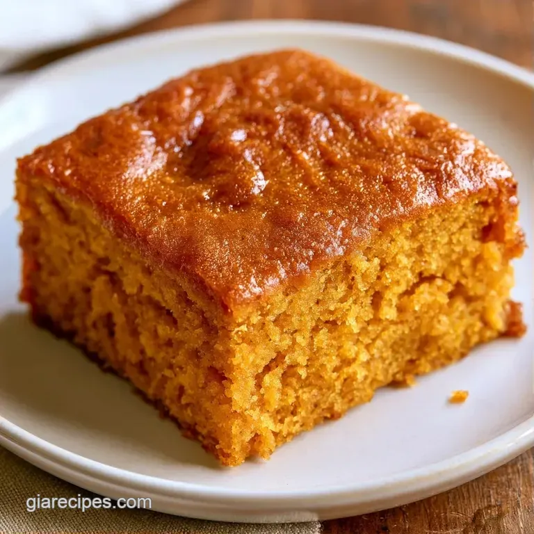 A square slice of moist pumpkin cake on a white ceramic plate, drizzled with maple syrup and fresh mint leaves.