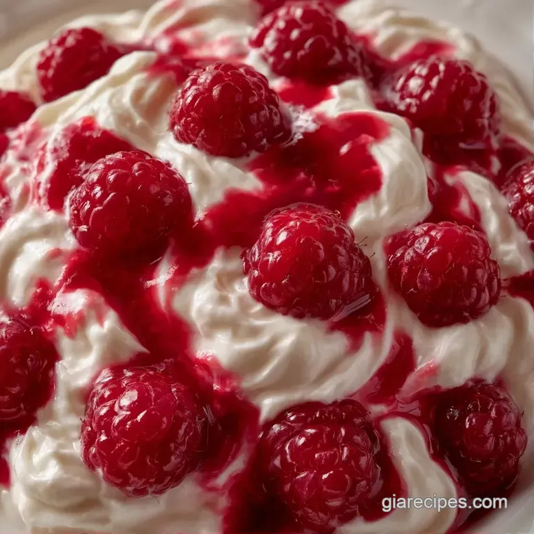 Layered dessert in a chilled glass with swirls of red raspberry sauce, fluffy cream, and white meringue shards.