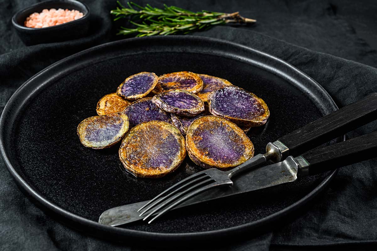 Vibrant purple sweet potatoes roasted and served with herbs on a rustic plate