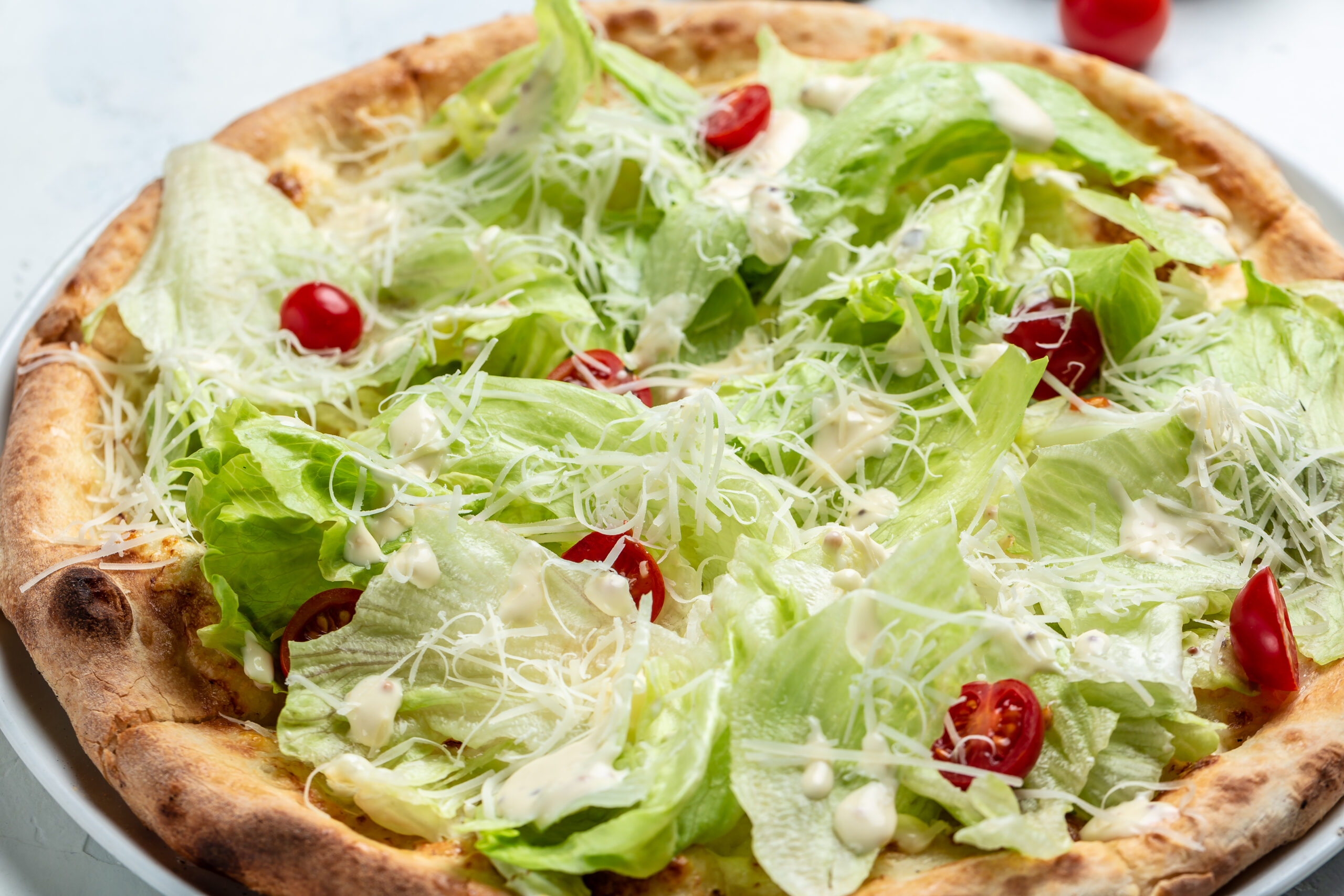 A freshly baked chicken crust Caesar salad pizza topped with romaine lettuce, Caesar dressing, and Parmesan cheese.